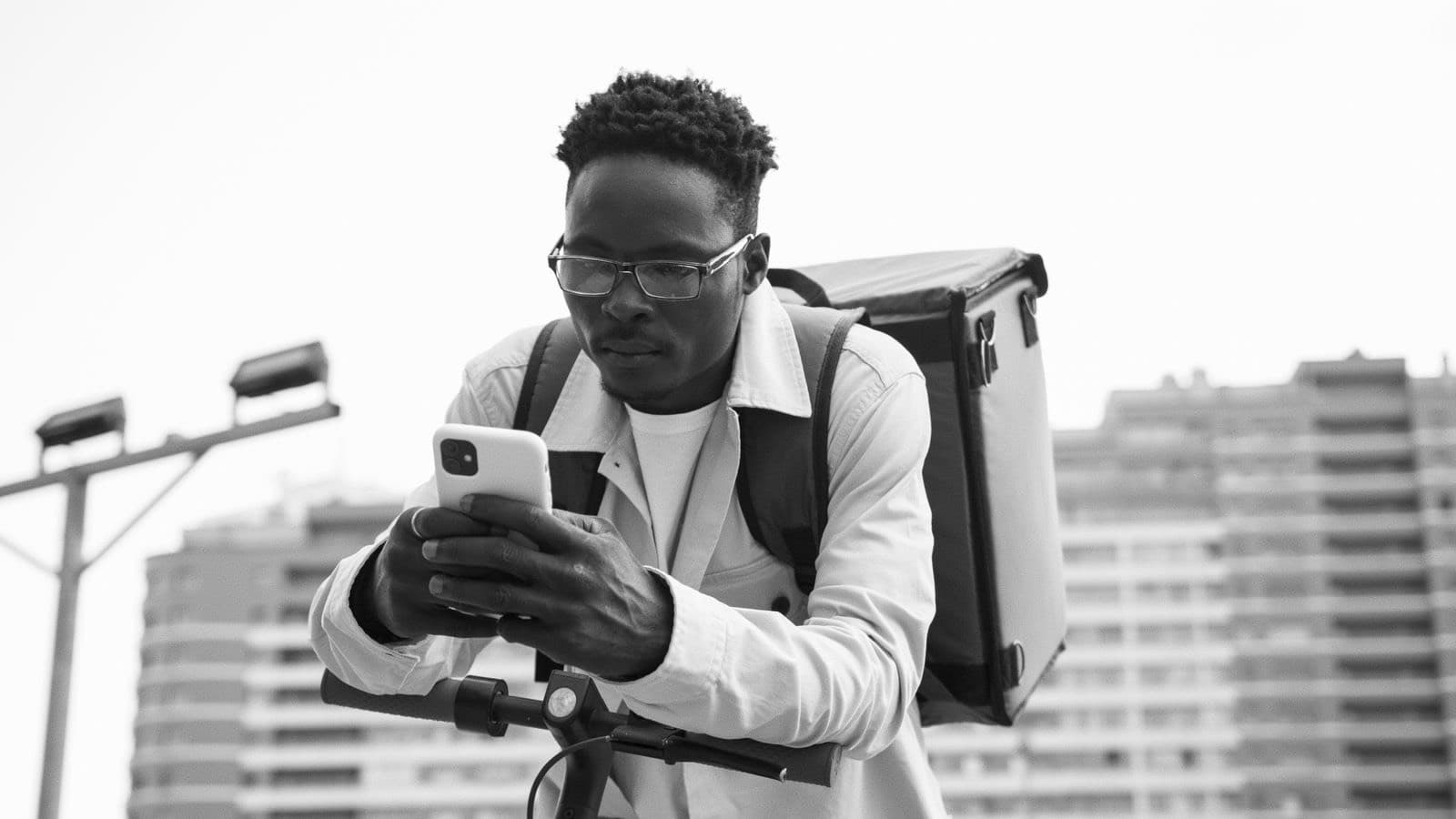 A delivery rider leans on the scooter handlebars, checking a phone between jobs.