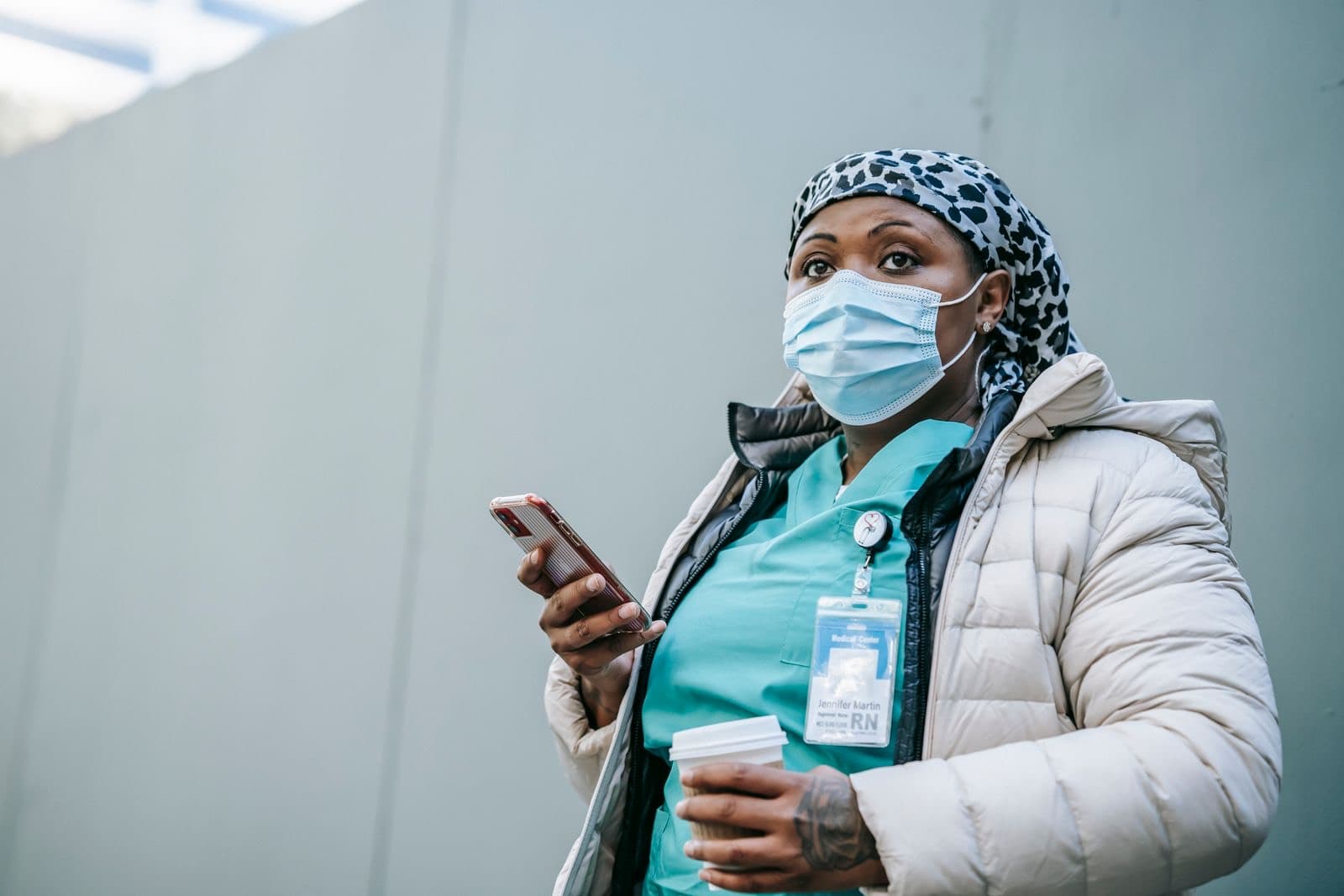 A nurse on a break outside, a phone in one hand and a coffee in the other.
