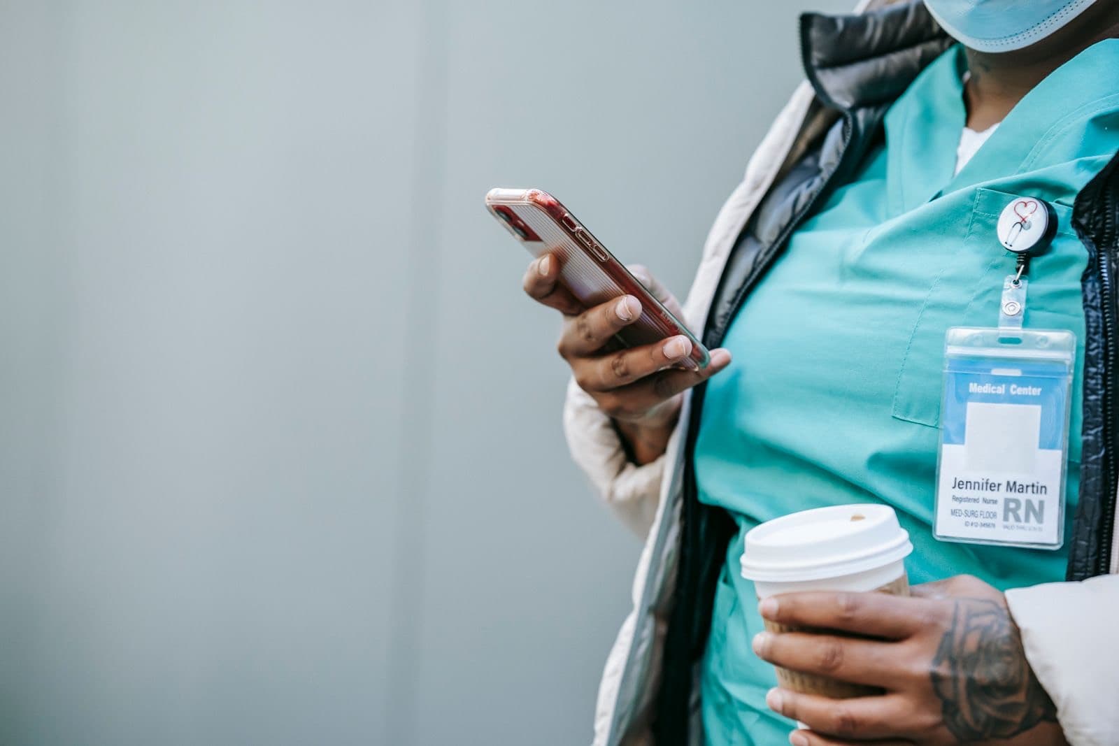 A nurse holds a takeaway coffee and checks her phone.